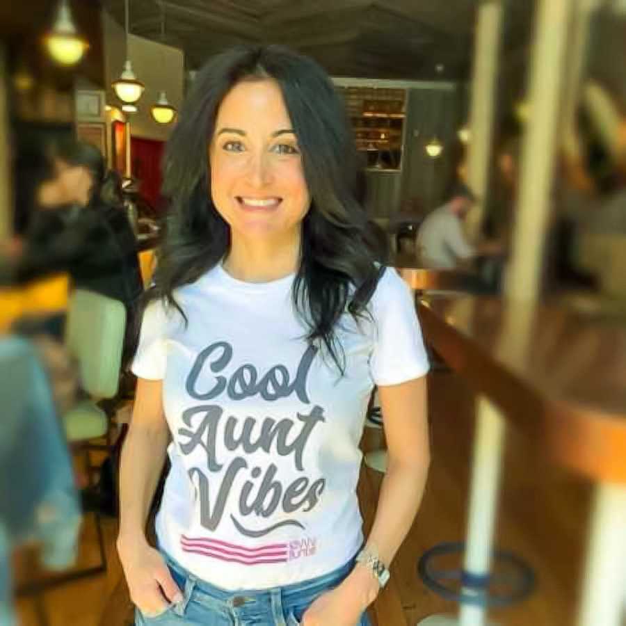 Woman who suffered a miscarriage stands smiling in t-shirt that says,"Good aunt vibes"