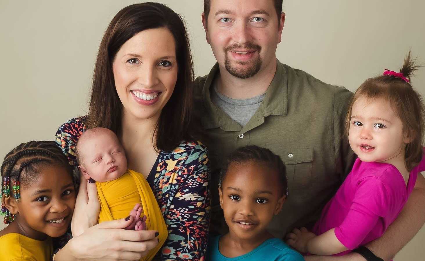 Husband and wife smile with their two birth children and two adopted children