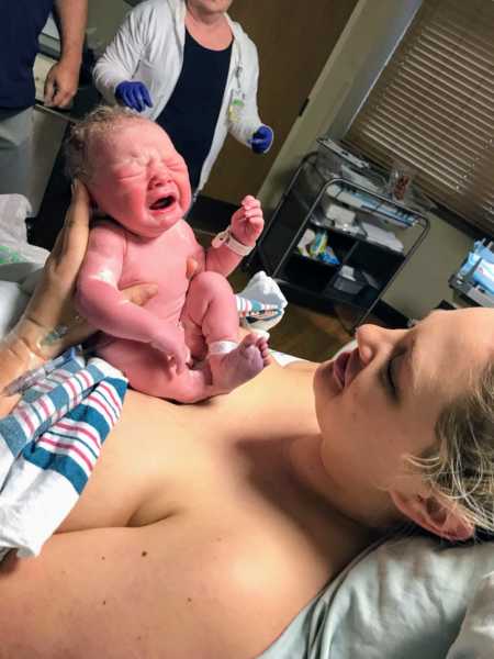 Newborn baby sits on mother's bare lap whose soldier father flew in hour after birth