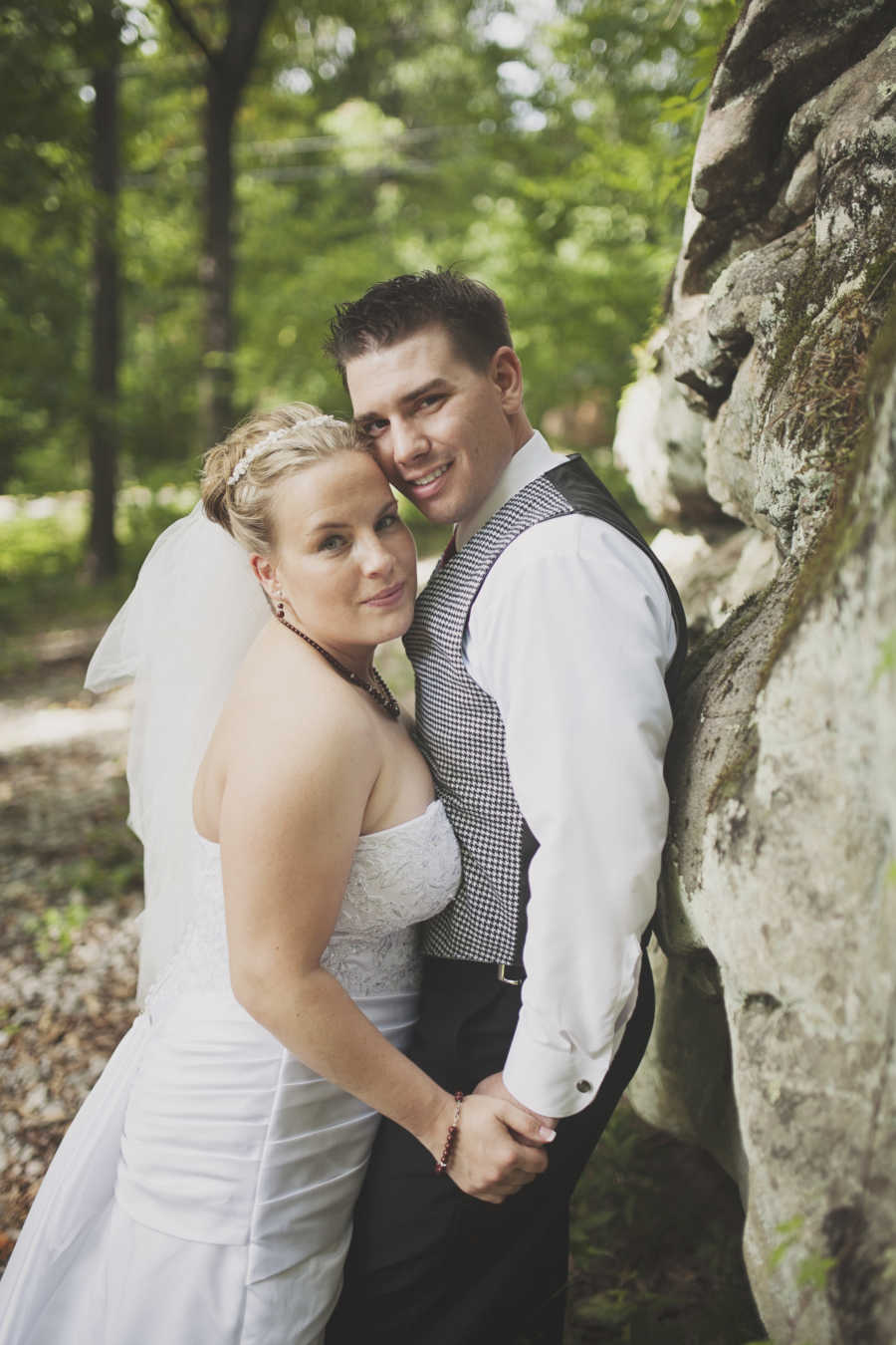 Bride and groom who met at Enterprise car rental hand in hand leaning against cliff wall