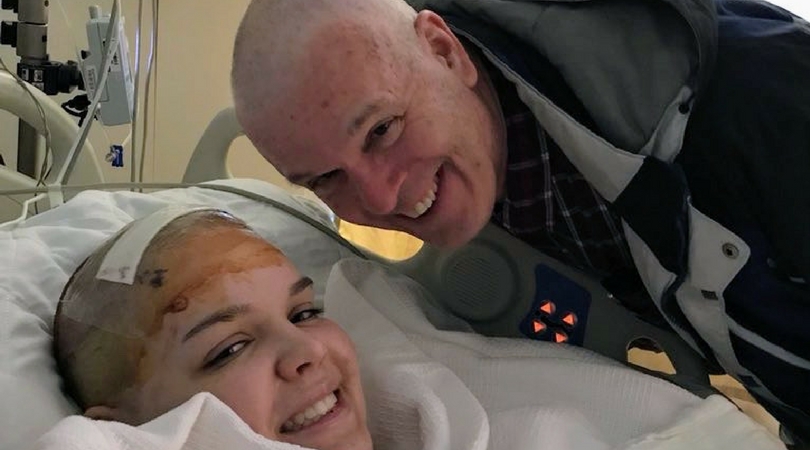 girl and dad smile with shaved heads in hospital