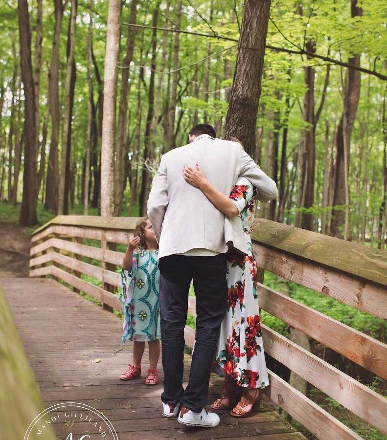 Man who just proposed stands hugging fiancee with her daughter beside them