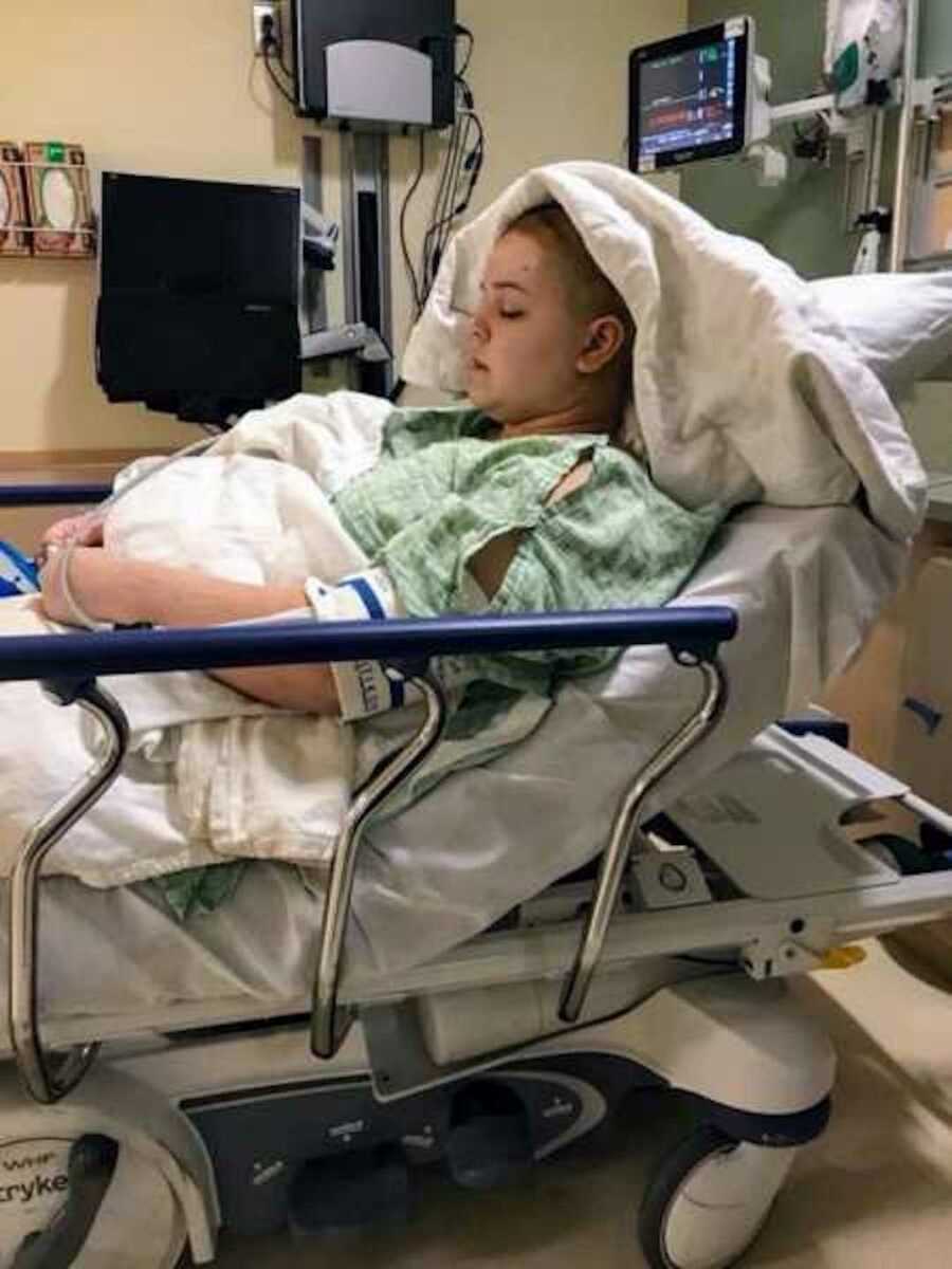 woman sits in hospital bed with shaved head