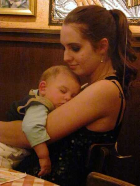Teen mom sitting at restaurant with infant son asleep in her lap