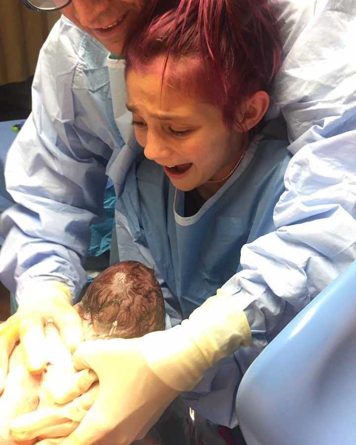 12 year old smiling at birth of newborn sibling in father's arms