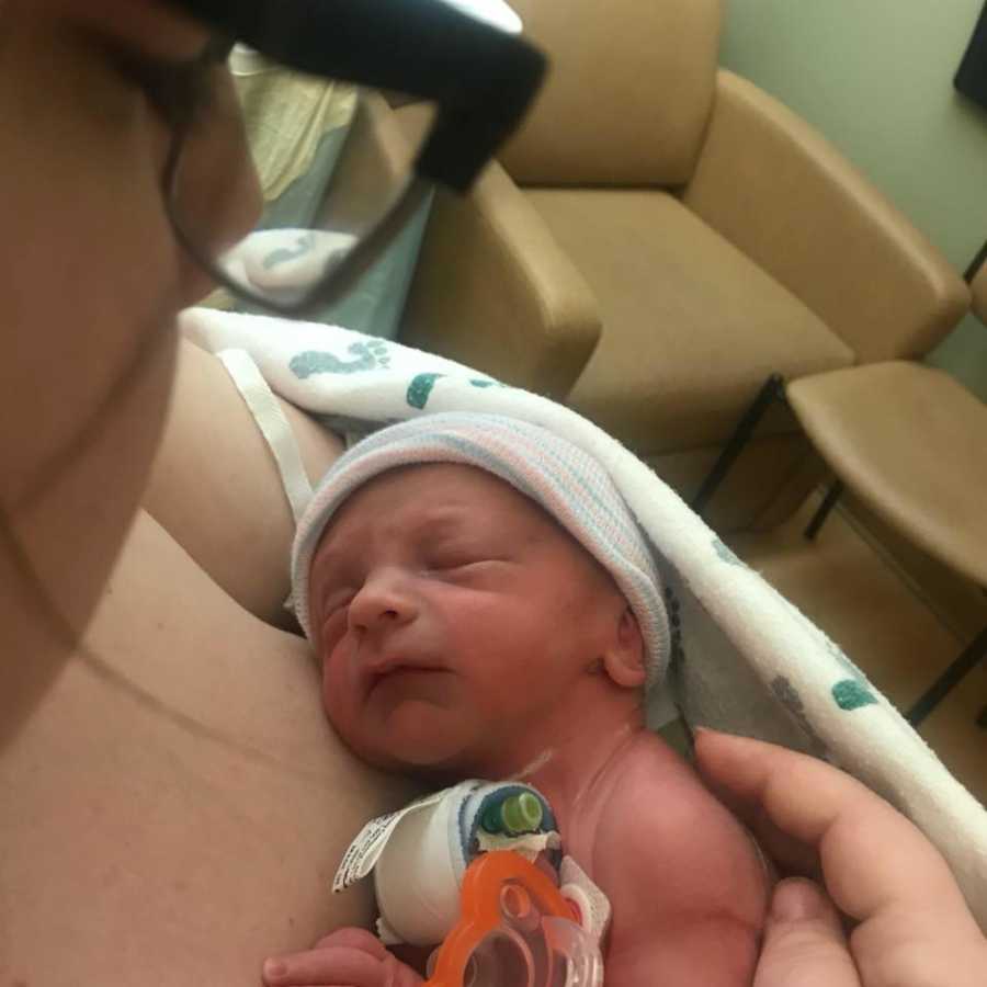 A mom holds her newborn baby who wears a cap and has a breathing tube