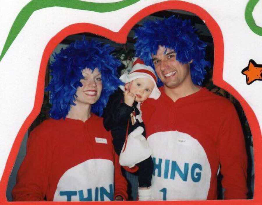 Parents dressed as Thing 1 and Thing 2 hold up their child dressed as Dr. Seuss's Cat in the Hat.