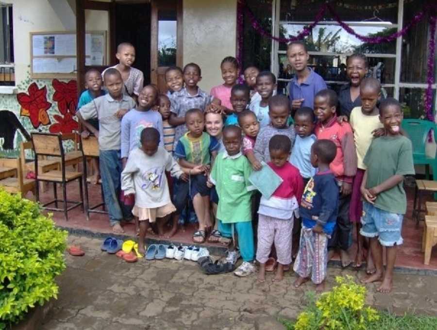 Woman crouches down outside orphanage in Africa surrounded by orphans