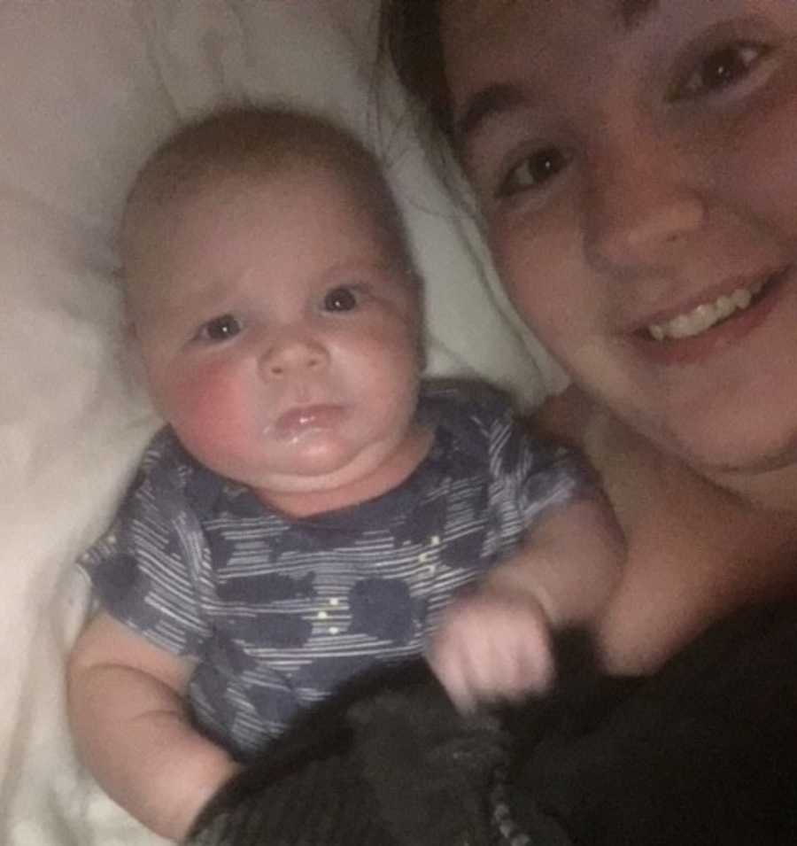 A mom lies next to her young baby who is wearing a blue shirt with fish on it.