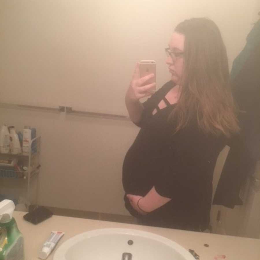 A pregnant woman in a black shirt takes a picture sin the mirror.