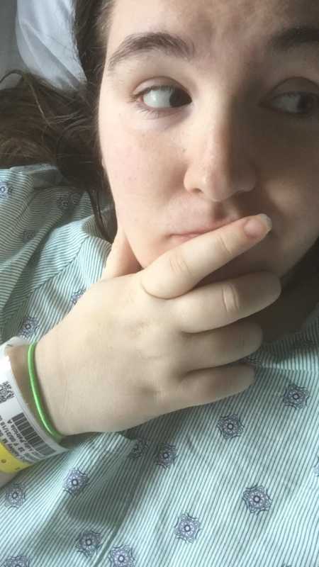 A mom wearing a hospital bracelet and hospital gown holds her fingers on her chin