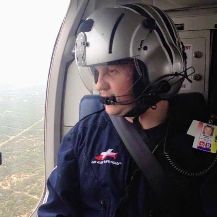 A man waring a helmet sits in a helicopter above trees and roads