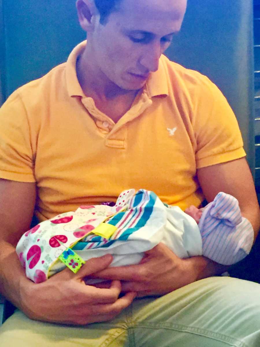 A dad wearing a yellow shirt holds his newborn baby girl