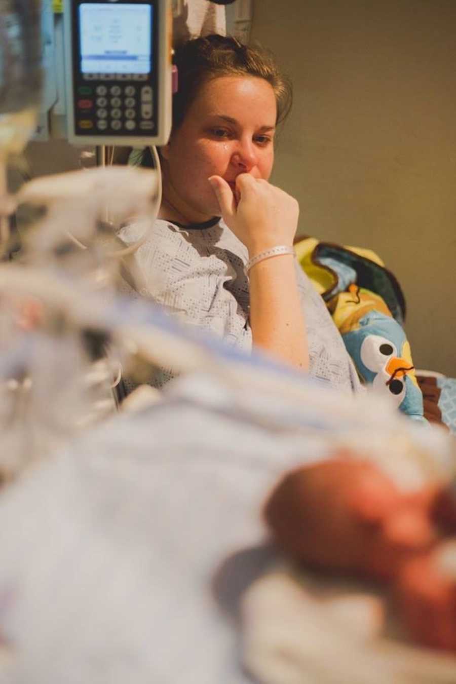 A mom watches tearfully as her newborn is treated in the hospital.