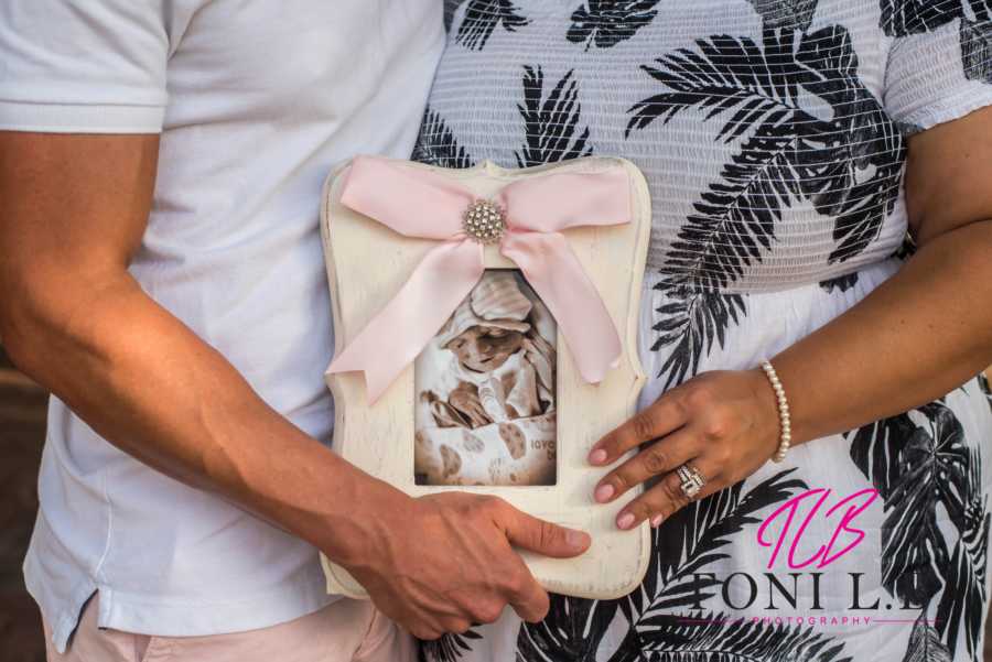 Parents hold a picture of their newborn baby in a frame