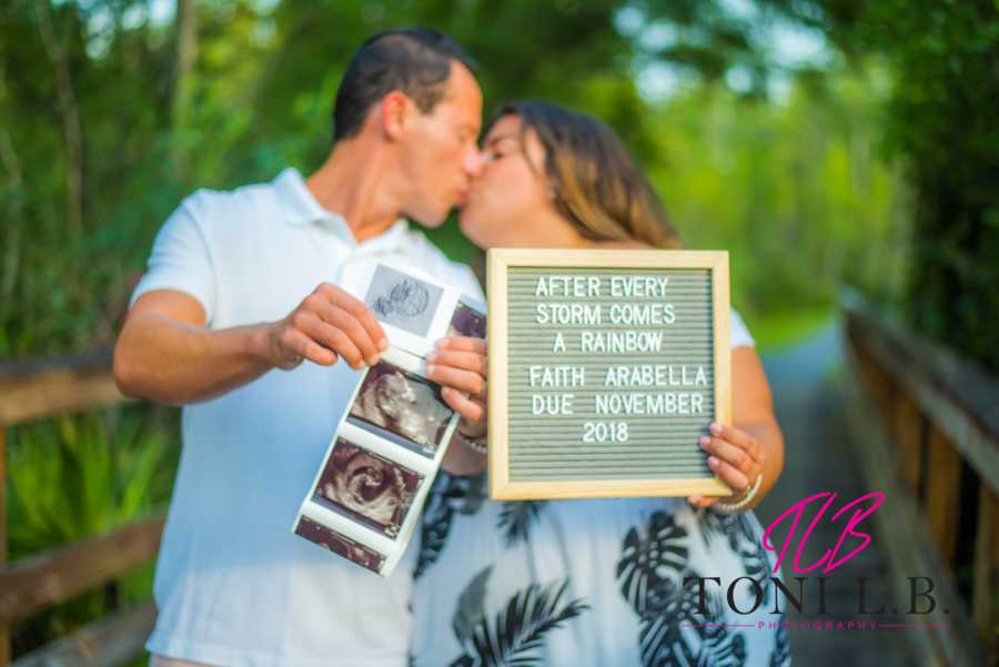 A couple kissing while holding out a sign and photos of their new baby