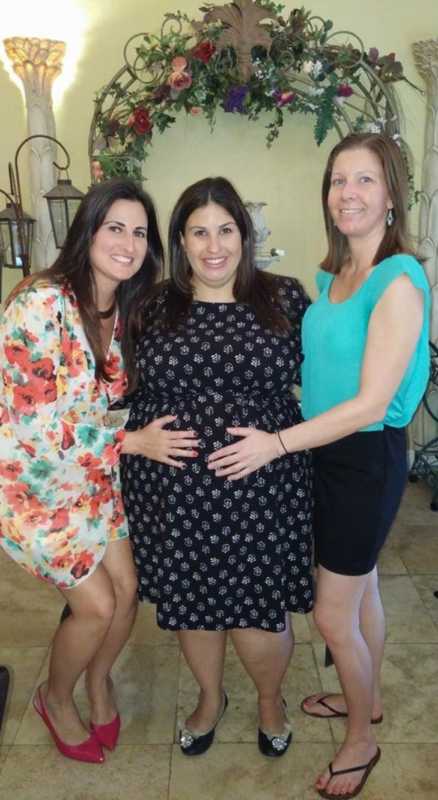 Two women place their hands on a pregnant woman's stomach