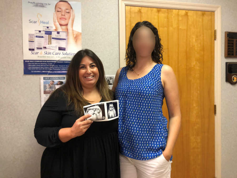 A mom holds an ultrasound picture while standing next to a tall woman in a blue shirt