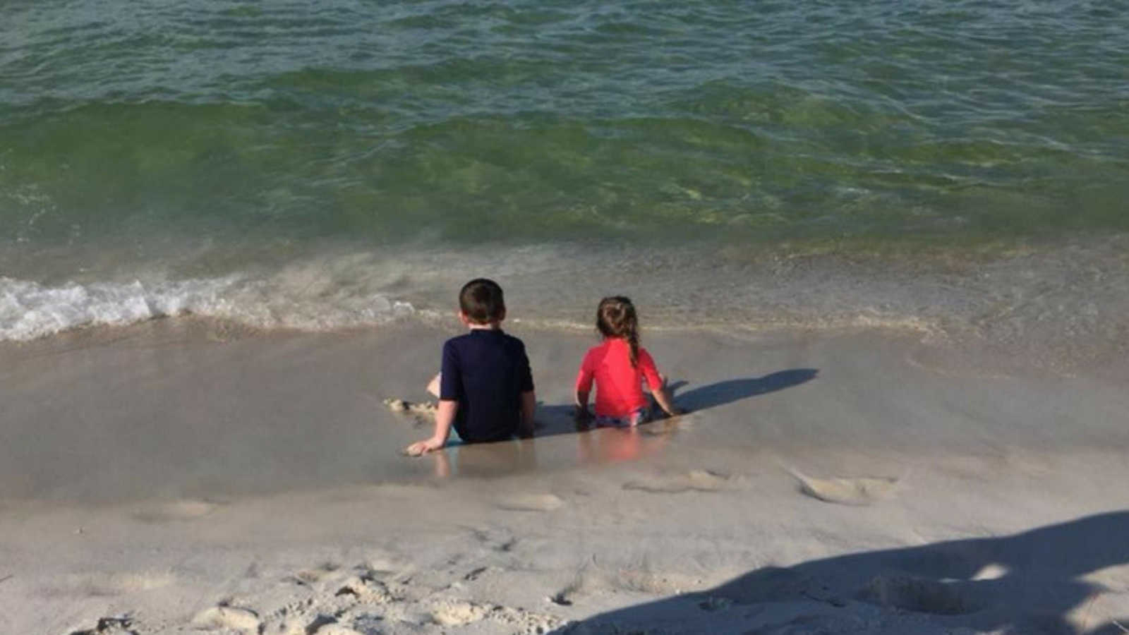 brother and little sister sit in the waves at the beach
