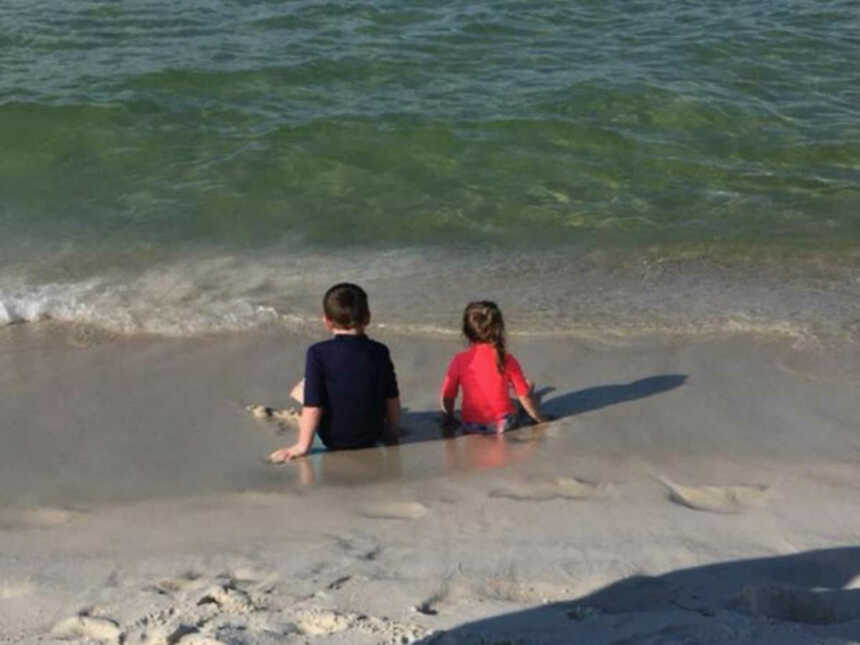 brother and little sister sit in the waves at the beach