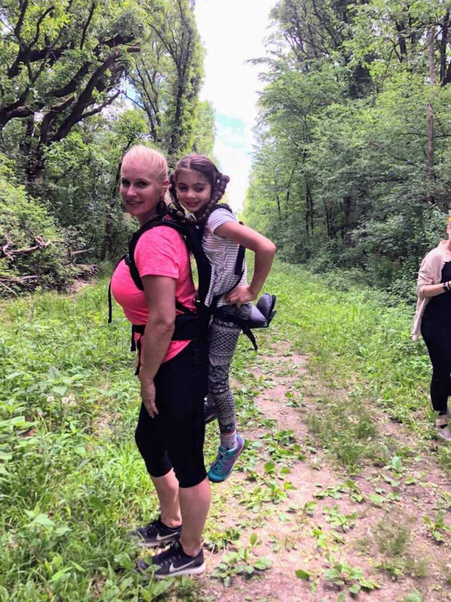 Smiling teacher holds girl with cerebral palsy on back