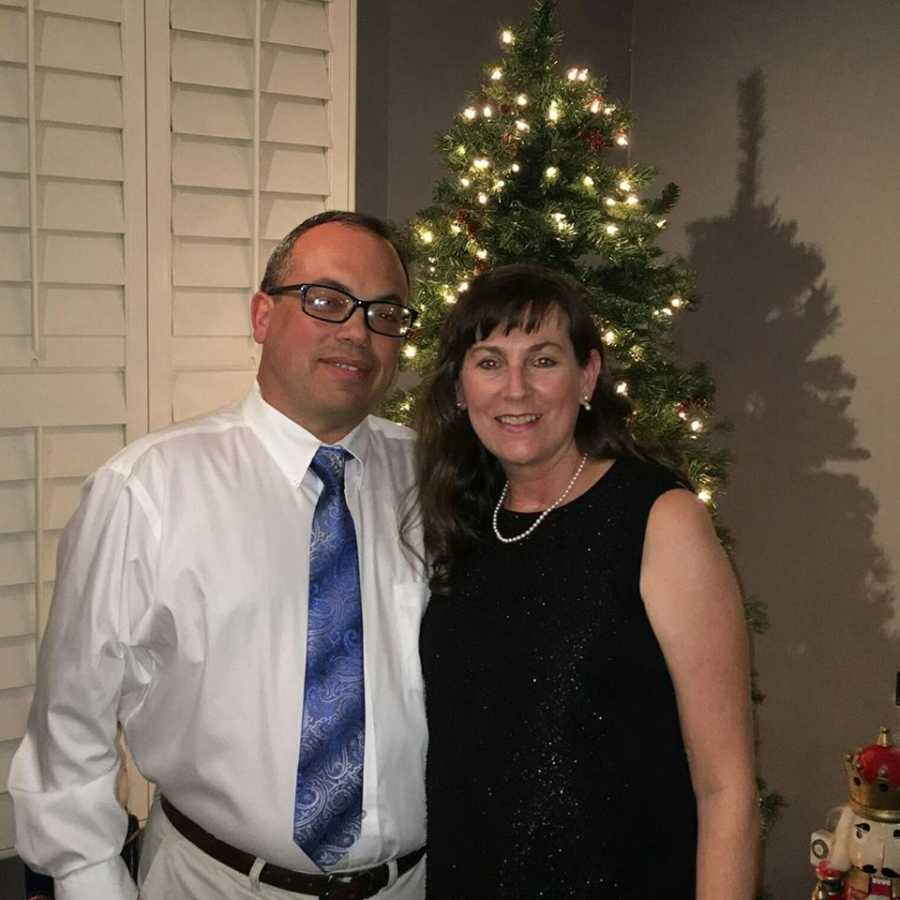 Married couple pose for a photo together while wearing fancy clothes in front of their Christmas tree