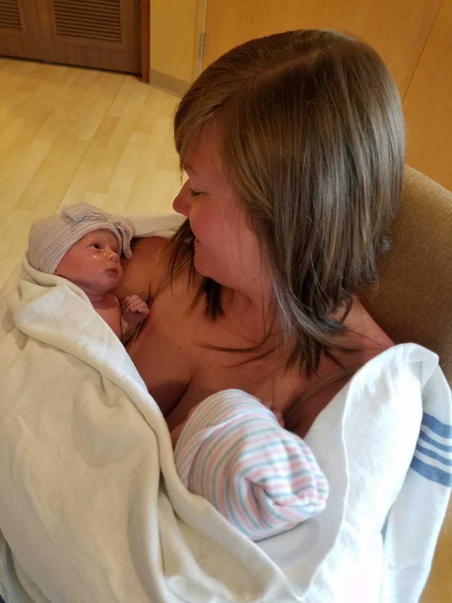Mom smiles down at her newborn twins while holding both of them