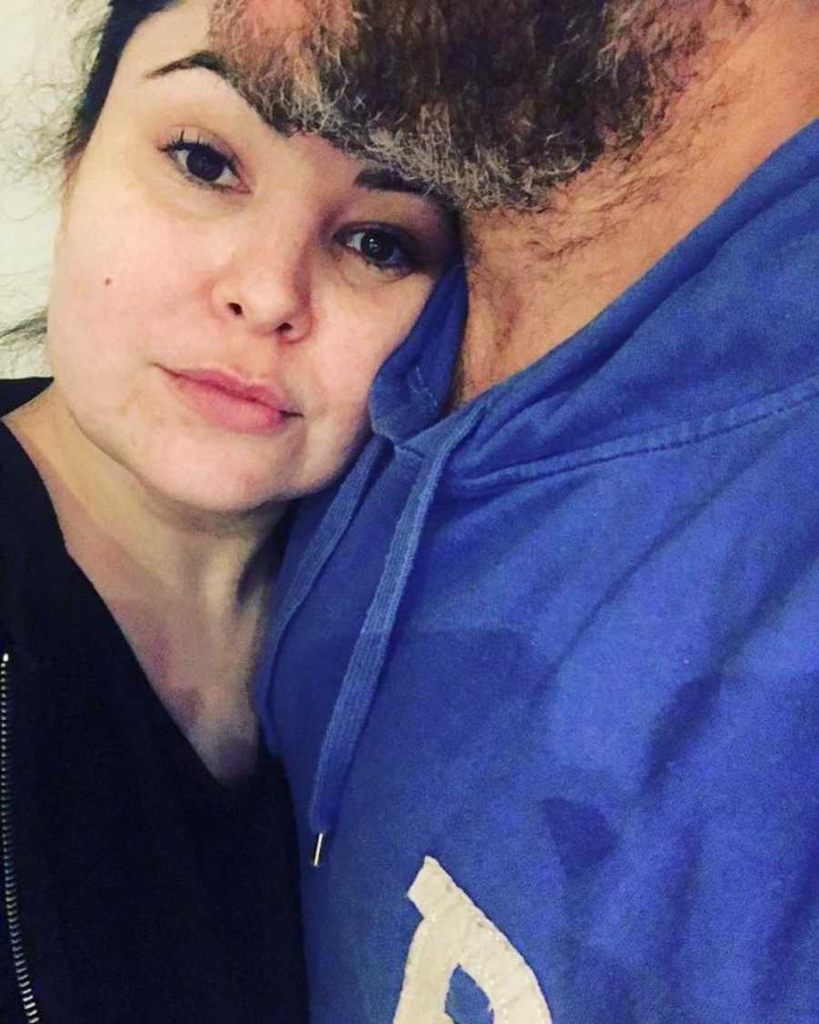 Woman takes selfie looking serious and solemn while laying on husband's chest