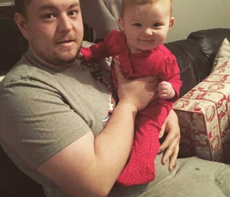 Dad holds chunky baby while they unwrap presents at Christmas