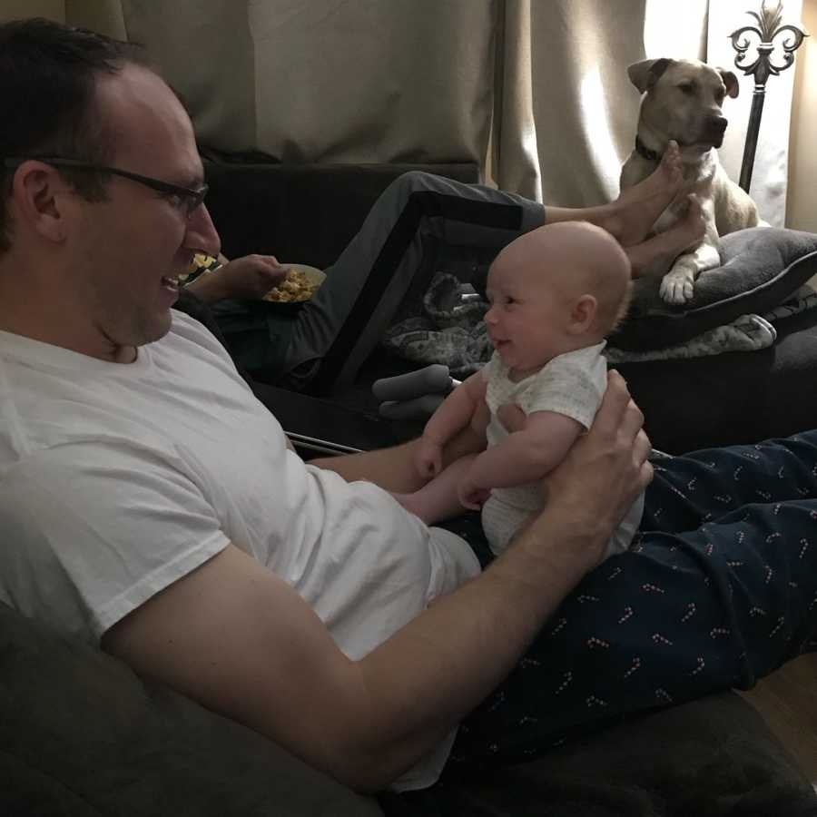 Father holds his newborn baby while they play together on the couch