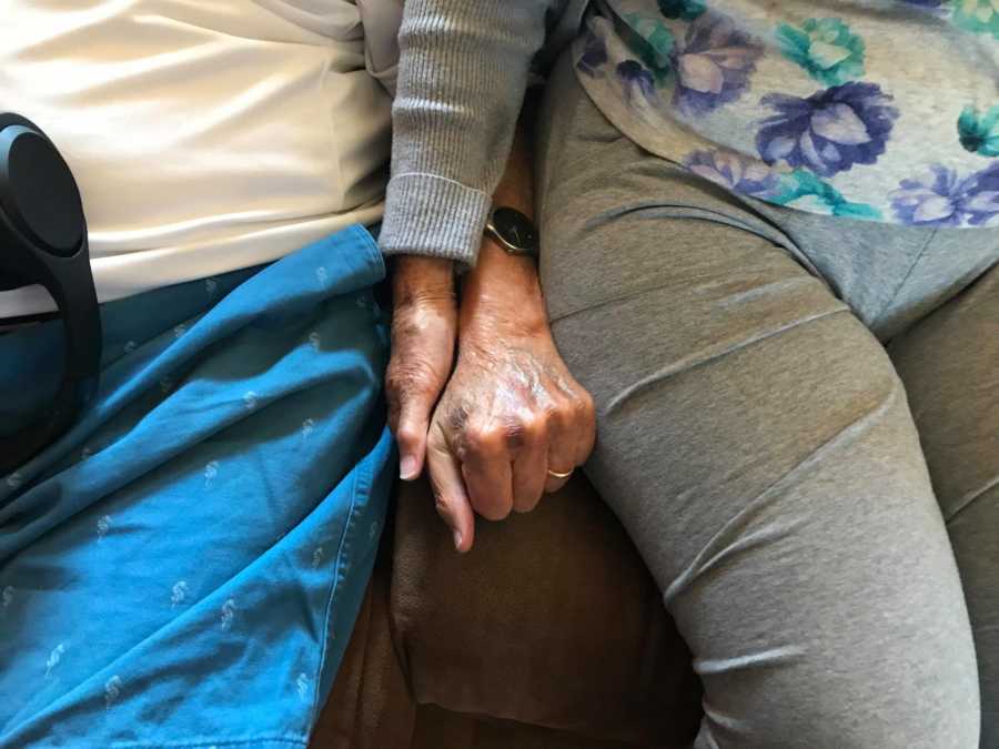 Elderly couple battling dementia together hold hands on the couch