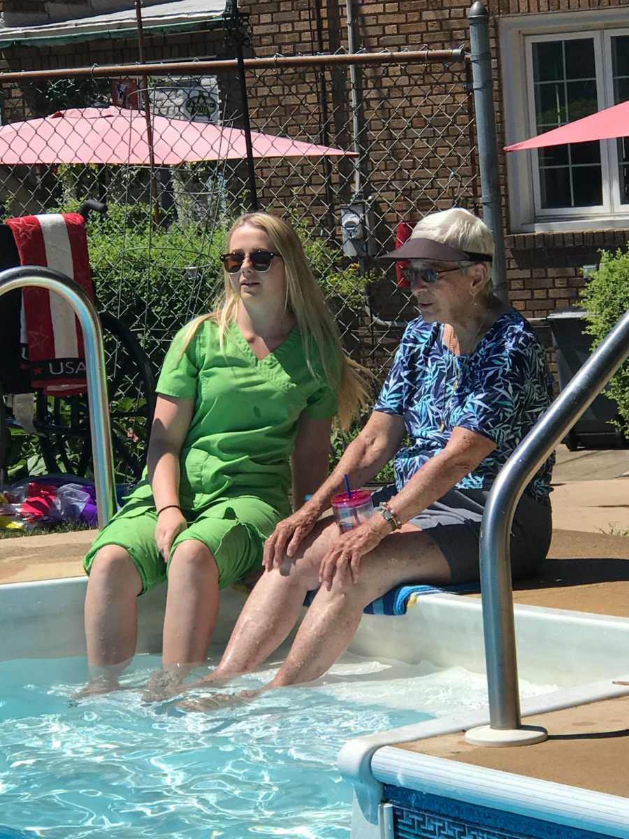 Woman with dementia sticks her feet in the water of a pool with a younger relative