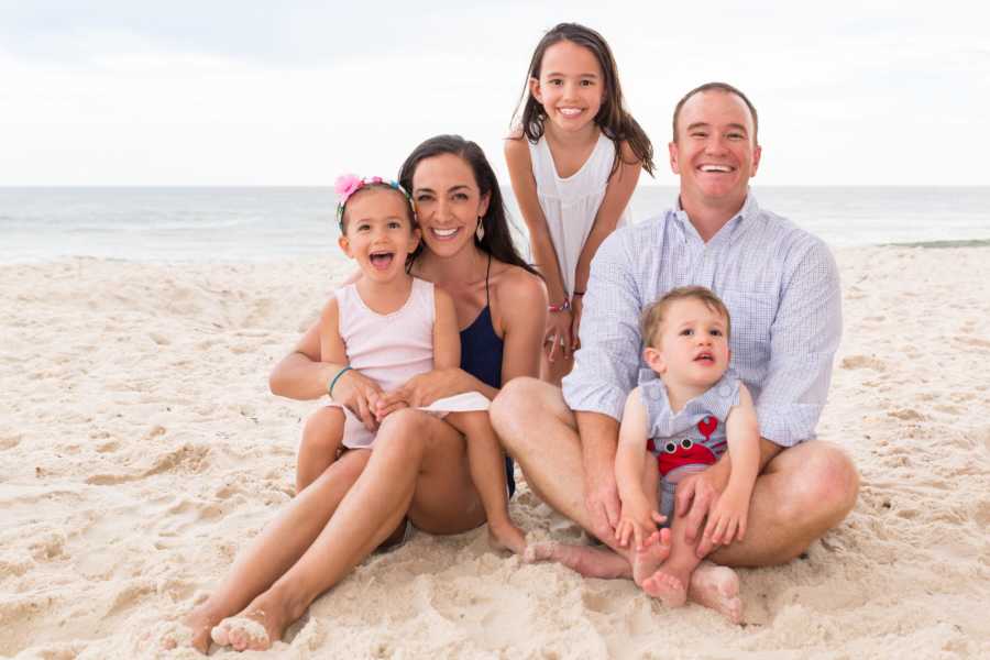 Family of five smile for a photo together while enjoying a day out on the beach