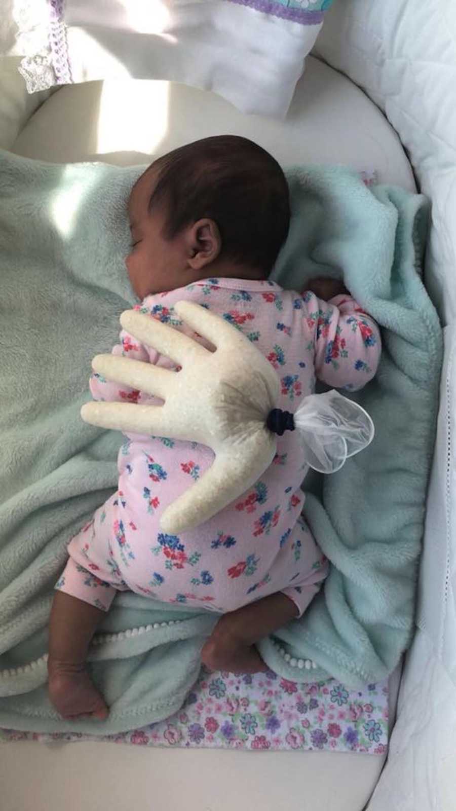 Newborn sleeps peacefully in her bassinet with a glove filled with rice on her back