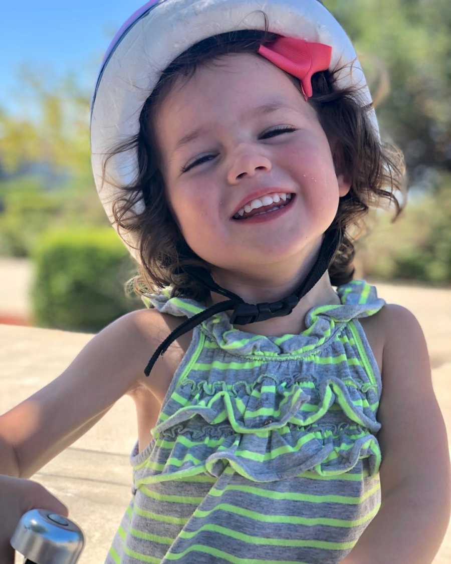 Strong-willed daughter smiles and laughs while riding her scooter and wearing a helmet