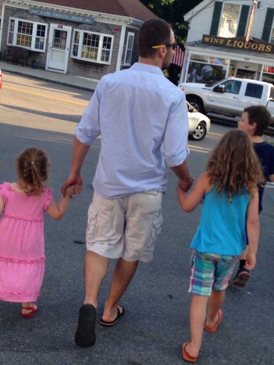 Dad walks hand in hand through a parking lot with his two daughters