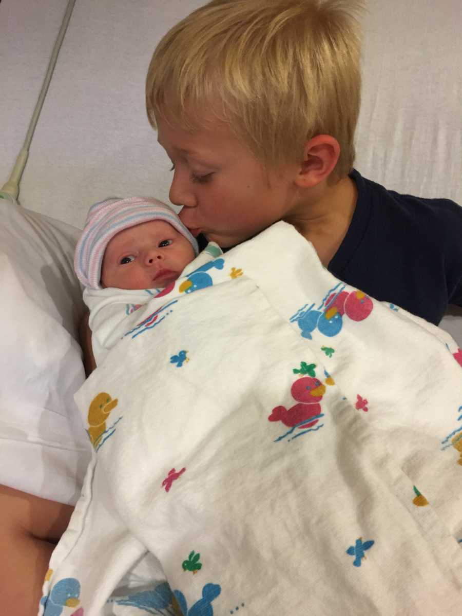 Older brother kisses his newborn sibling on their forehead