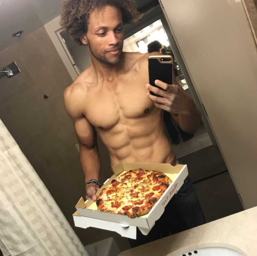 Muscular man takes a shirtless mirror selfie while holding a pizza