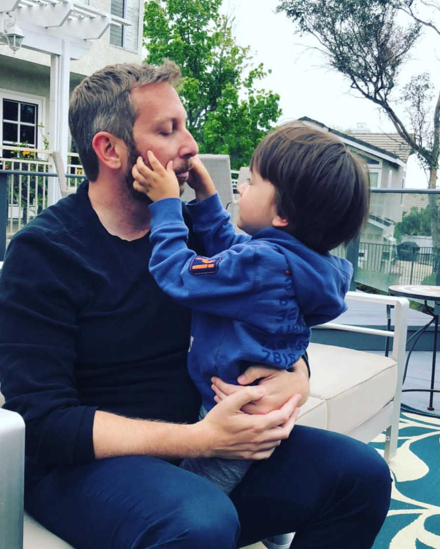 Little boy plays with his father's mustache while sitting outside at a restaurant