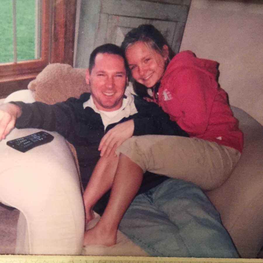 Preteen daughter sits with her dad in their living room sofa chair