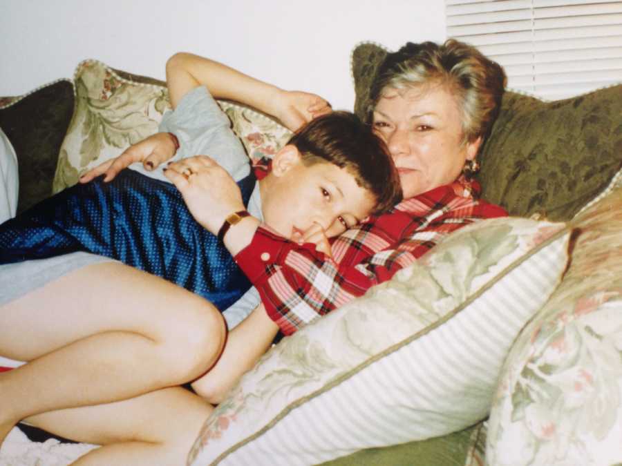 Young boy sucks his thumb while cuddling with his grandmother on the couch