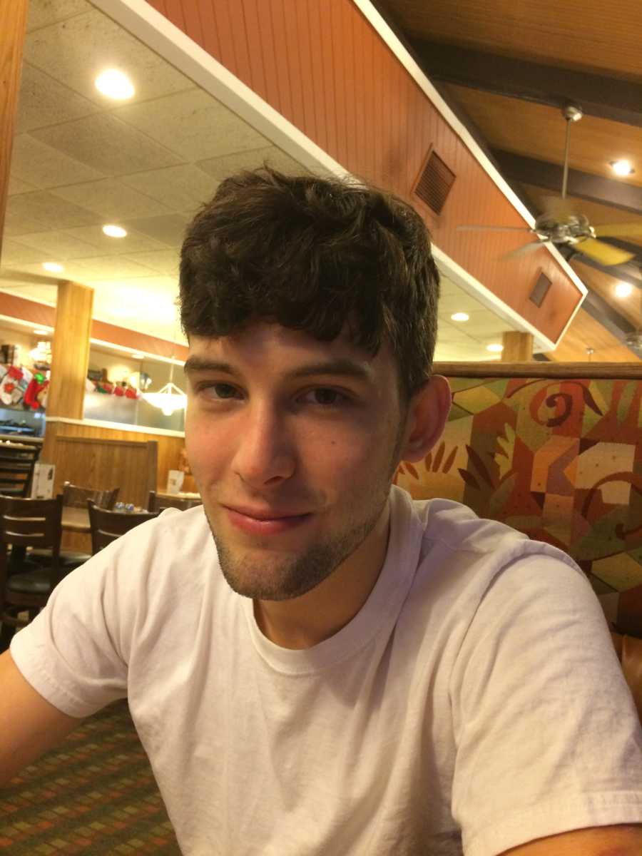 Young man who has recovered from drug addiction sits in booth smiling at restaurant