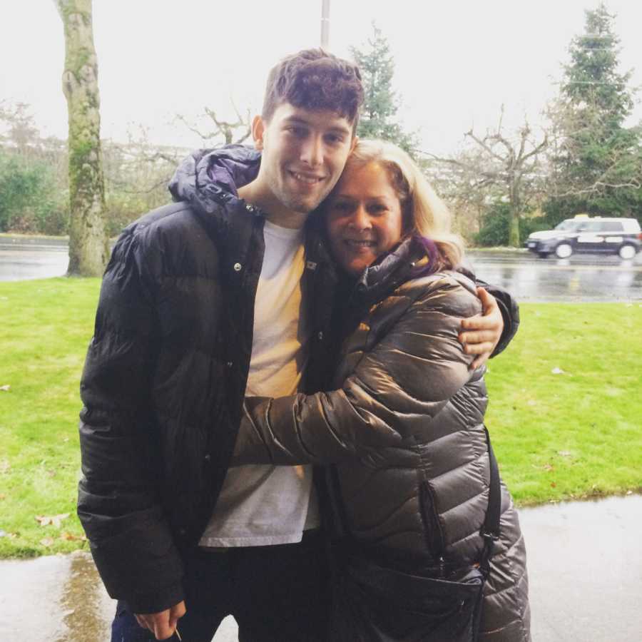 Mom hugs her son for a quick photo in matching puff jackets while it rains behind them