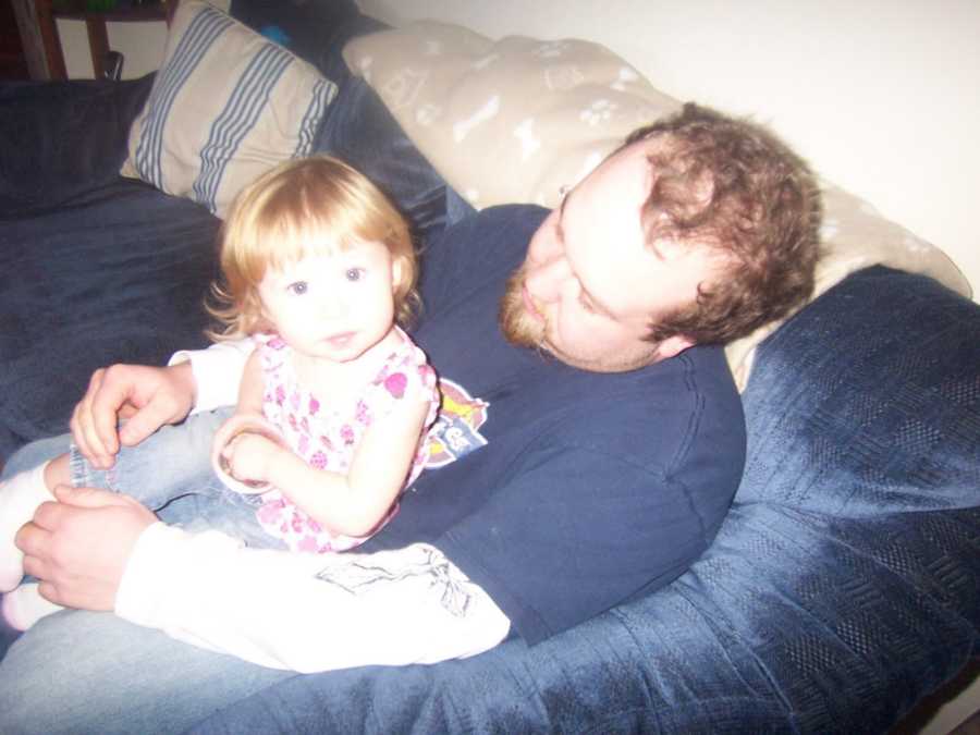 Father holds his toddler daughter on a blue couch