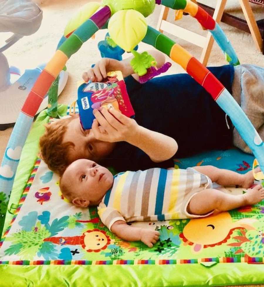 Big brother reads to his little brother while they lay on a playmat together