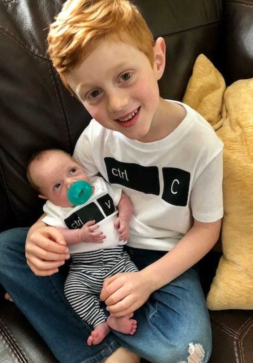 Brothers wear matching t-shirts while cuddling on the couch