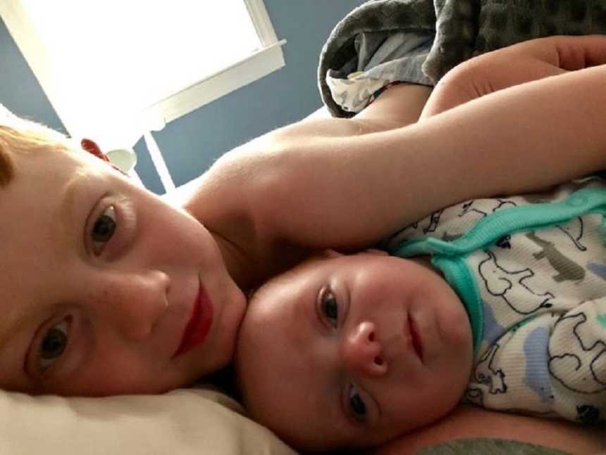 Big brother takes a selfie while cuddling his newborn brother