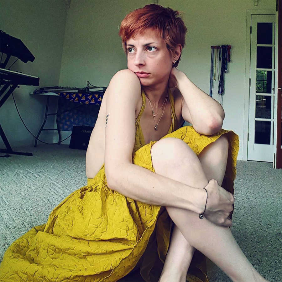 Woman looks serious for a photo while sitting on the floor in a yellow dress