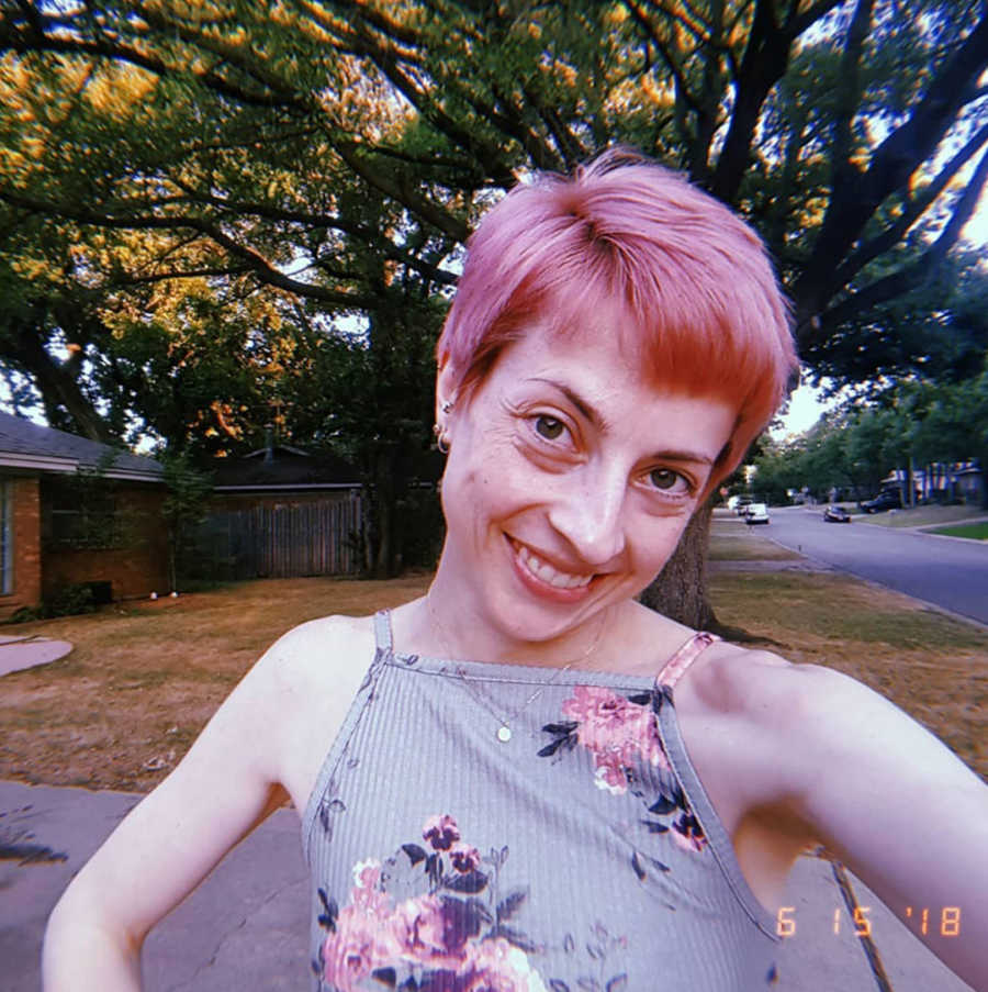 Woman recovering alcoholism takes a selfie in her front yard with pink pixie cut and floral tank top