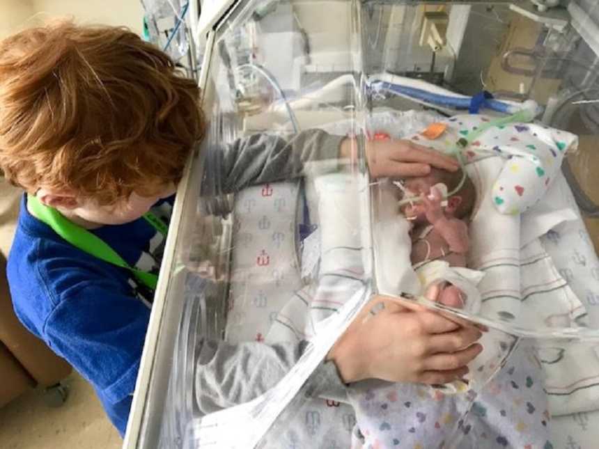 Big brother touches his newborn brother in his NICU bassinet